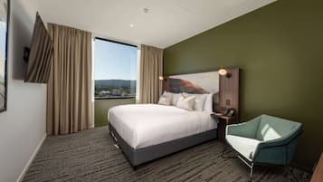 A hotel room with a large bed, a view of the city, a green wall, and a modern chair.