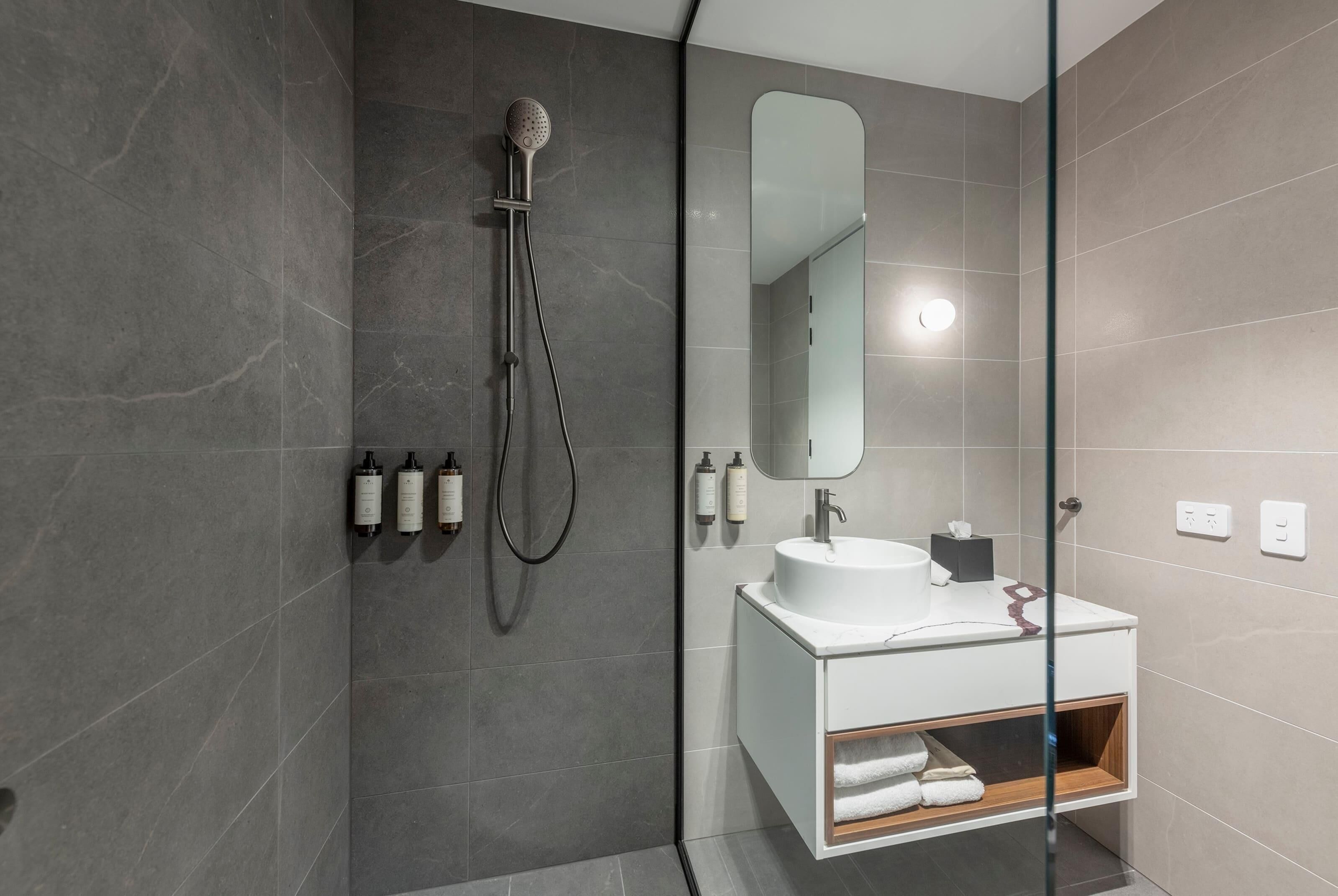 A modern bathroom with a glass-enclosed shower, a white sink, and a mirror above it.