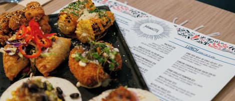 A menu with various lunch options and a plate of food including tacos and a stuffed corn cob.