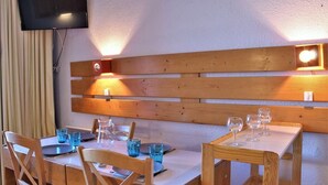 Un comedor con mesas y sillas de madera, un televisor montado en la pared e iluminación en la pared.