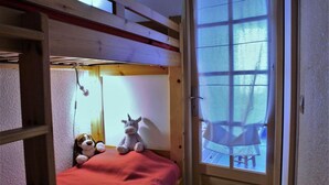 Una cama litera con colchón rojo, un peluche y una ventana con vistas al exterior.