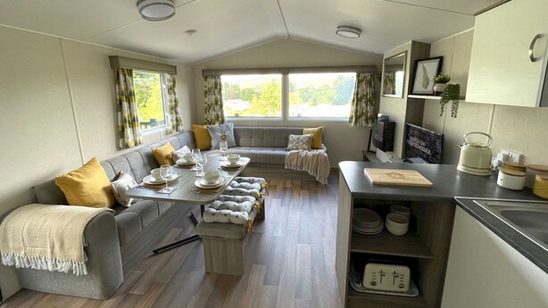 A cozy living area with a sofa, a dining table set for four, and a kitchen area with a kettle and a framed picture on the wall. - Beautiful 3BR Holiday Home in Stunning Location - Pass the Keys (Moffat)