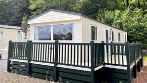 A mobile home with a fenced deck, surrounded by trees. - Beautiful 3BR Holiday Home in Stunning Location - Pass the Keys (Moffat)