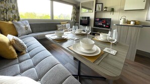 A modern interior with a sofa, dining table set for four, a TV, and a kitchen area. - Beautiful 3BR Holiday Home in Stunning Location - Pass the Keys (Moffat)