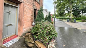 En murstensbygning med en grå dør og en lille have med sten og planter.