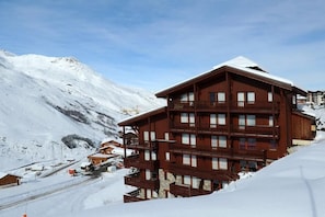 Un edificio de madera de varios pisos con balcones, con una montaña nevada al fondo.