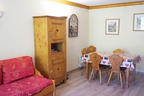 Una habitación con un armario de madera, un sofá rojo, una mesa de comedor con sillas y cuadros en la pared.