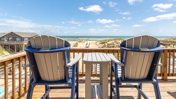 Two Adirondack chairs facing a wooden deck with a view of the beach and ocean. - Anchored at Last - S Nags Head MP 19.5, Oceanfront, Pool, Hot Tub, Kiddie Pool, Pool Table (Nags Head)