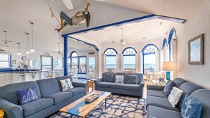 A spacious living area with a large sofa set, a coffee table, and a view of the ocean through arched windows. - Anchored at Last - S Nags Head MP 19.5, Oceanfront, Pool, Hot Tub, Kiddie Pool, Pool Table (Nags Head)