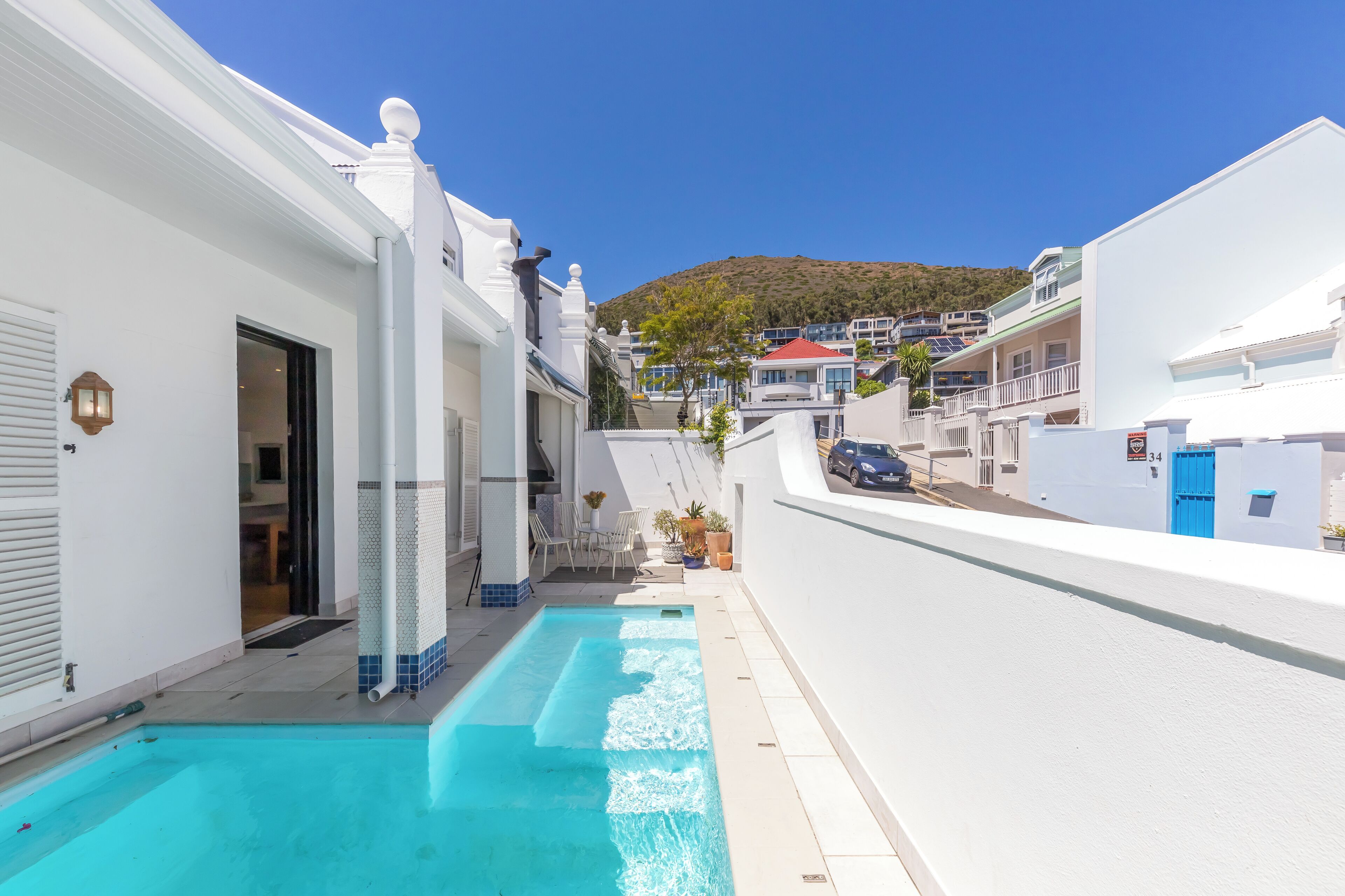 Uma área residencial com piscina, edifícios brancos e uma colina ao fundo.