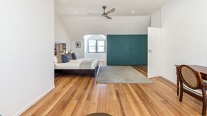 A spacious room with a wooden floor, a bed with pillows, a desk with a chair, and a teal wardrobe. - Spacious Modern Home in iconic Green Point (Cape Town)