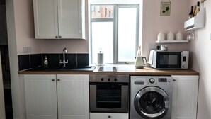 Cocina compacta con muebles blancos, microondas, lavadora y ventana con vistas a edificios.