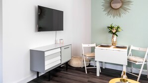 Un moderno comedor con una mesa y sillas blancas, un televisor montado y un espejo decorativo con diseño de sol en la pared.