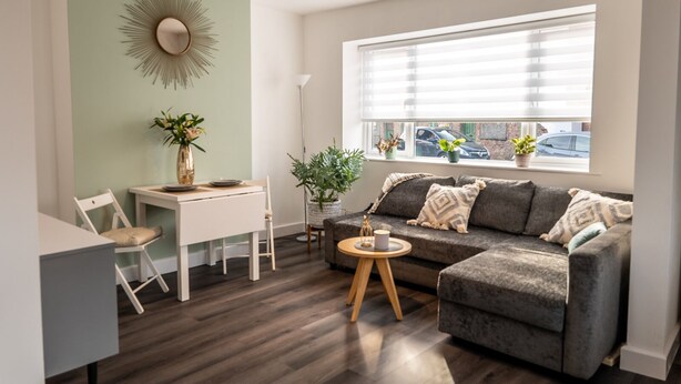 Un salón moderno con un sofá gris, una mesa de comedor y un amplio ventanal con persianas.