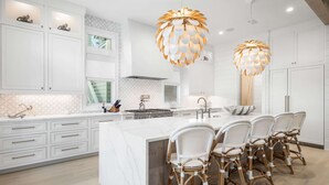 Une cuisine moderne avec des meubles blancs, un grand îlot central doté de tabourets et des luminaires suspendus originaux.