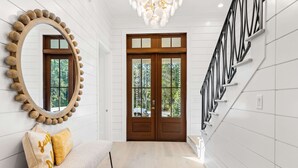 Un intérieur moderne avec une porte en bois, un miroir rond, un banc avec des coussins et un escalier.