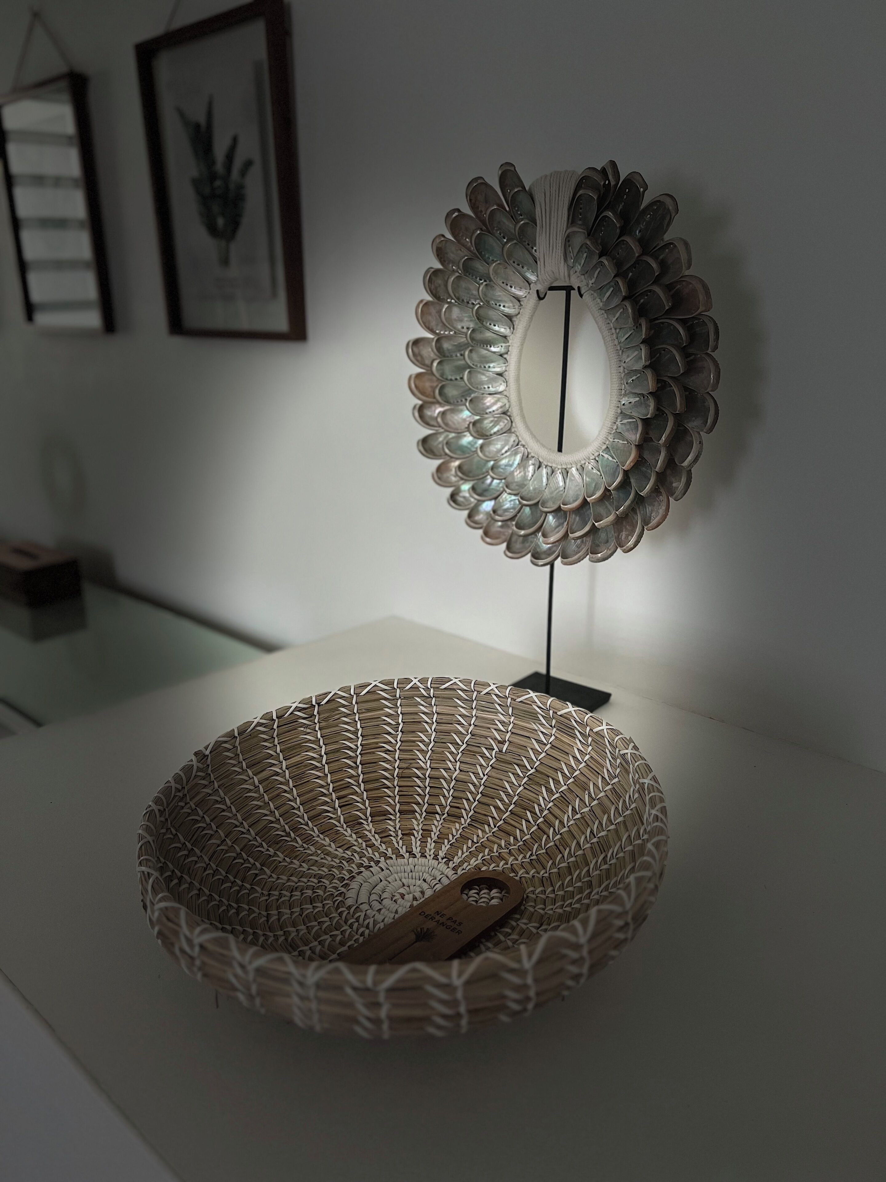 A decorative mirror with a scalloped edge, a woven basket, and a small wooden plaque with text.