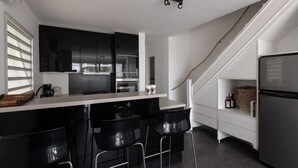 Eine moderne Küche mit schwarzen Barhocker, einem Edelstahlkühlschrank und einer Treppe zu einem Erkerraum.