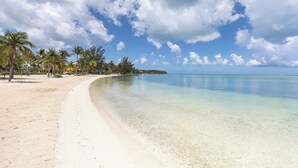 Ein Strand mit klarem türkisblauem Wasser, weißem Sand und Palmen unter einem teils bewölkten Himmel.