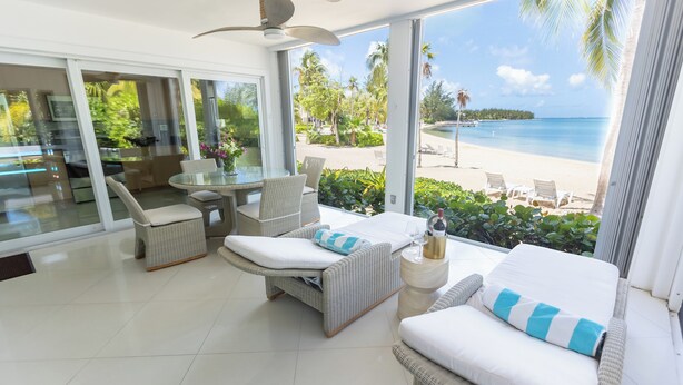 Ein modernes Zimmer mit einem großen Glasfenster, das einen Blick auf den Strand bietet, ausgestattet mit einer Couch, Sesseln und einem Tisch.