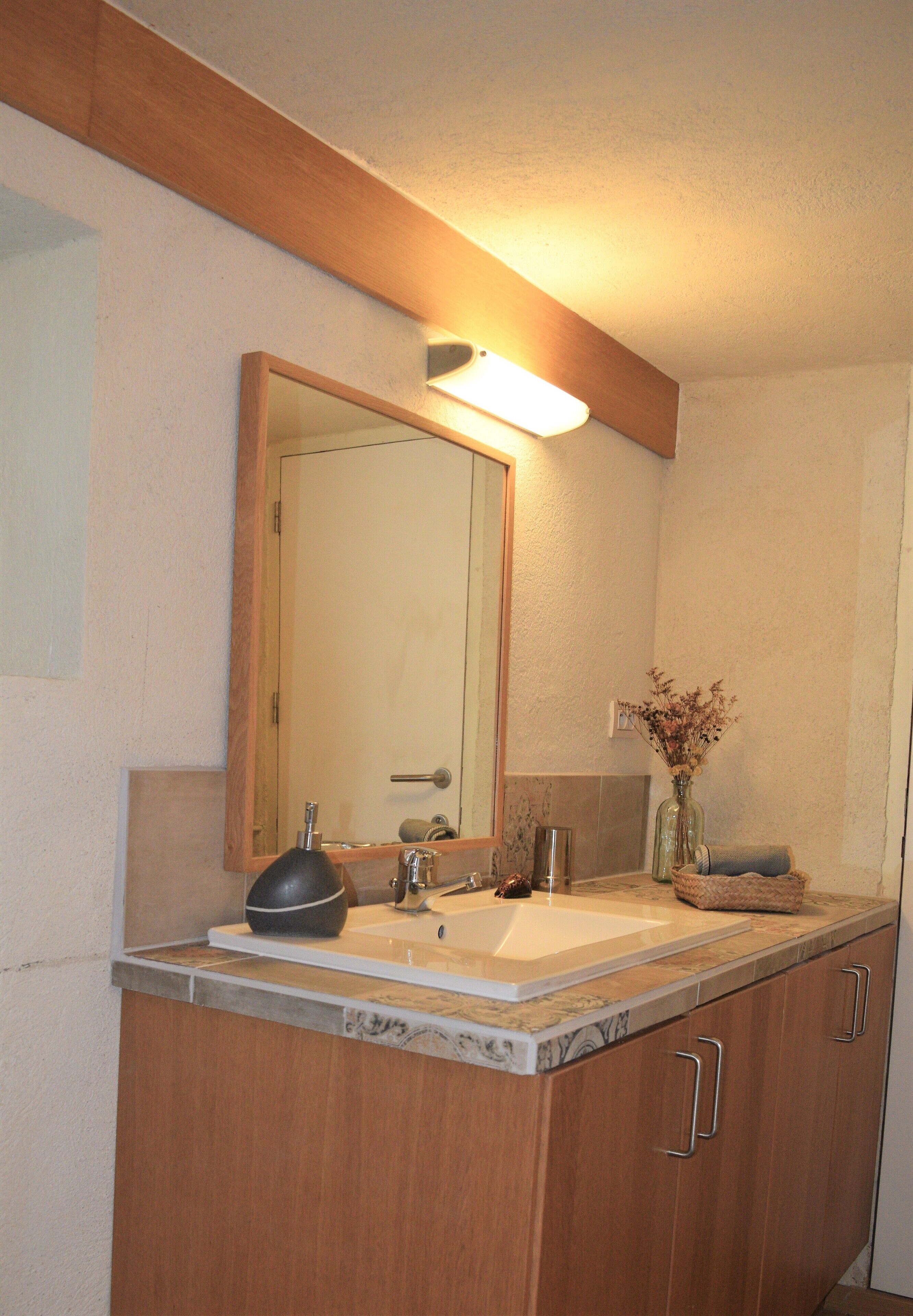A bathroom with a wooden vanity, two sinks, a mirror, and a vase with dried flowers.