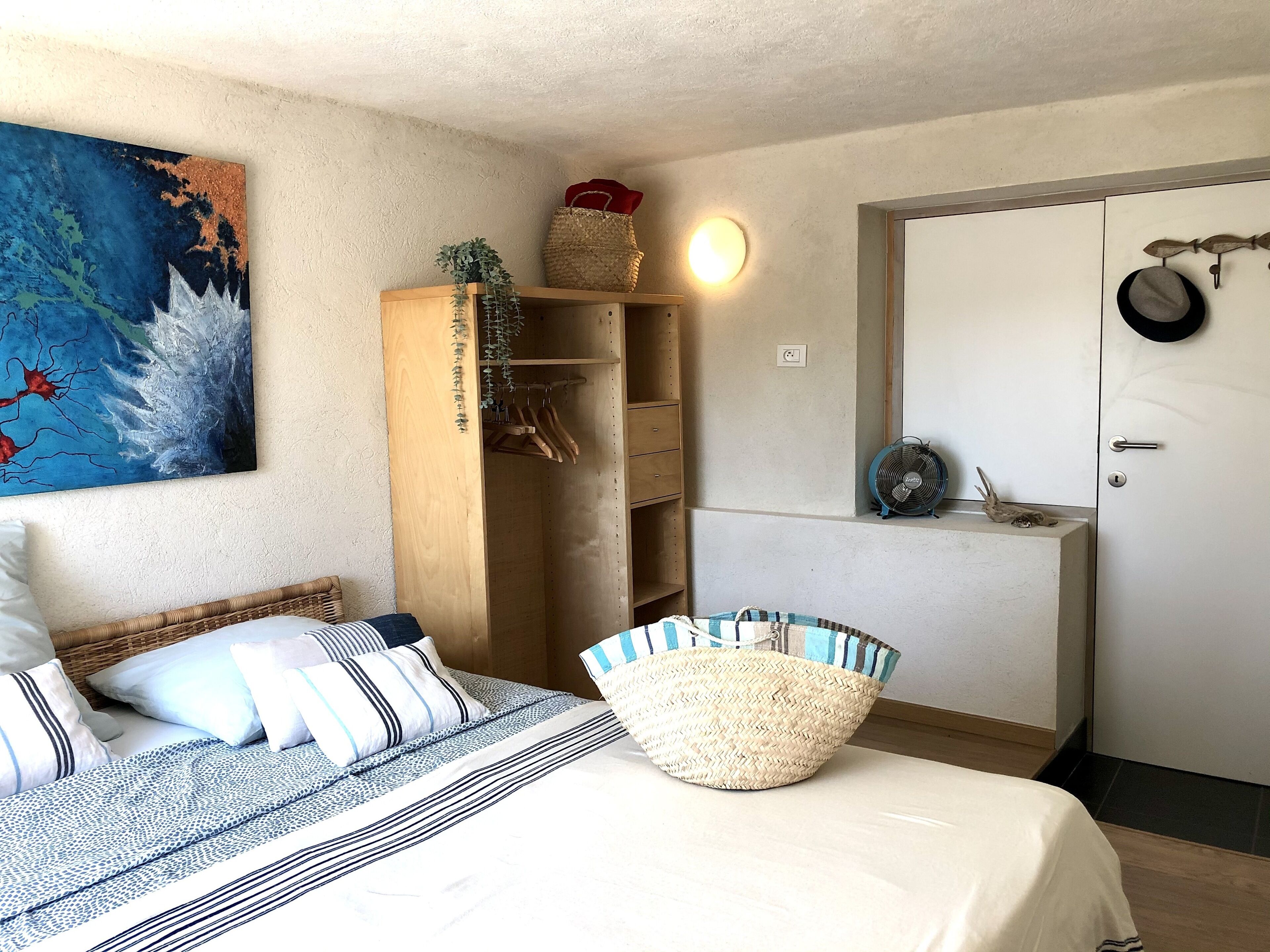 Une chambre à coucher avec un lit, une armoire, un bureau et une porte ornée d’un chapeau et d’un éventail.
