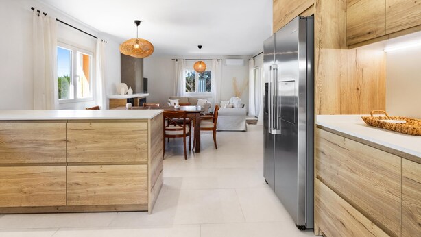 A modern kitchen with wooden cabinetry, a stainless steel refrigerator, and a dining area with a table and chairs. - Villa Gioia (Tolleric)