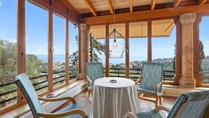 A sunlit patio with a round table and four chairs, large windows offering a scenic view, and a hanging light fixture. - Villa Genova (Palma de Mallorca)