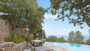 An outdoor pool area with stone walls, a table, and lounge chairs. - Villa Genova (Palma de Mallorca)