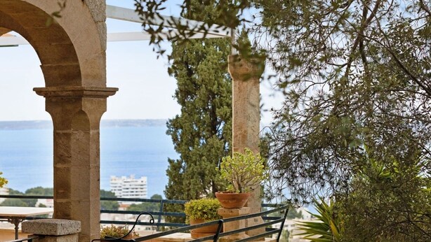 A balcony with a stone balustrade, potted plants, and a view of the sea. - Villa Genova (Palma de Mallorca)