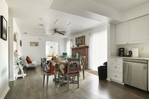 A dining area with a table and chairs, a kitchen with white cabinets and a dishwasher, and a ceiling fan.