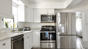 A modern kitchen with white cabinets, a stainless steel refrigerator, a microwave, and an oven.