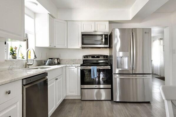 A modern kitchen with white cabinets, a stainless steel refrigerator, a microwave, and an oven.