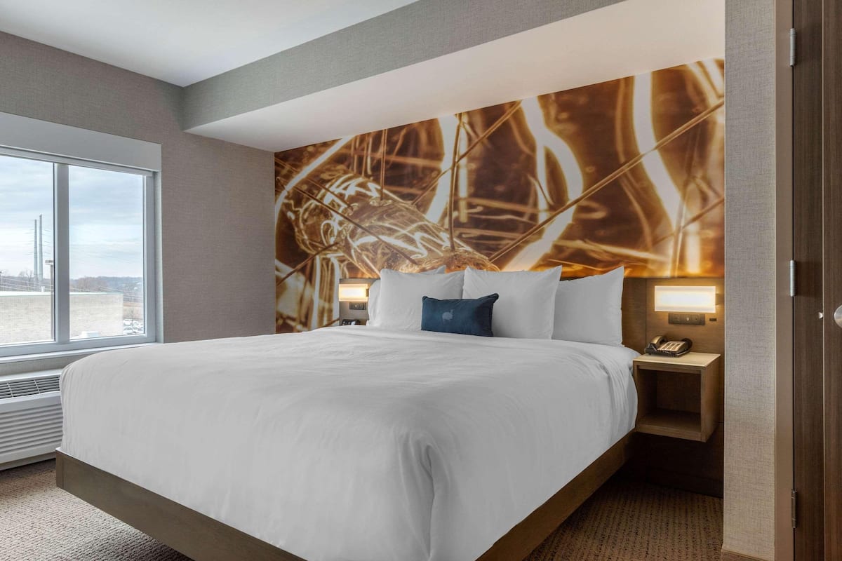 Quarto de hotel com uma cama grande, mesa de cabeceira com telefone e parede com padrão de folhas.