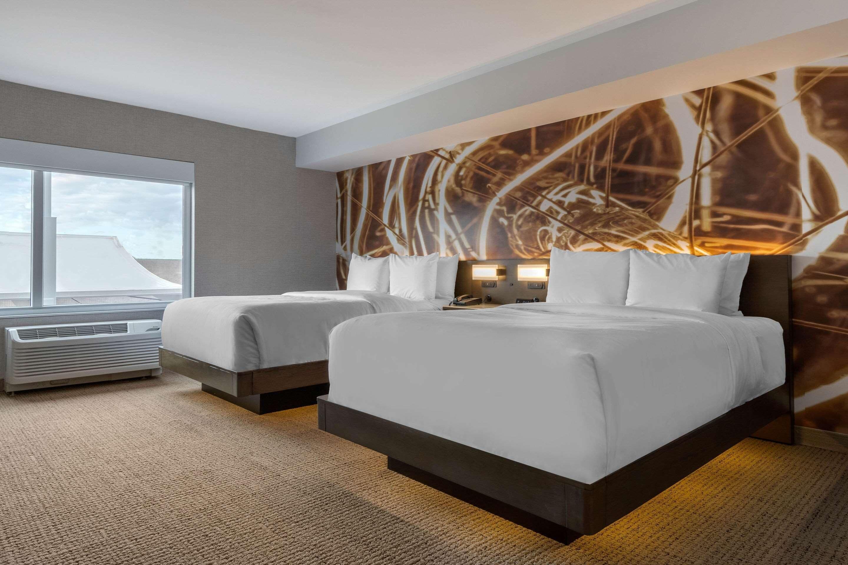 Une chambre d’hôtel avec deux lits, une grande fenêtre et une œuvre d’art accrochée au mur.