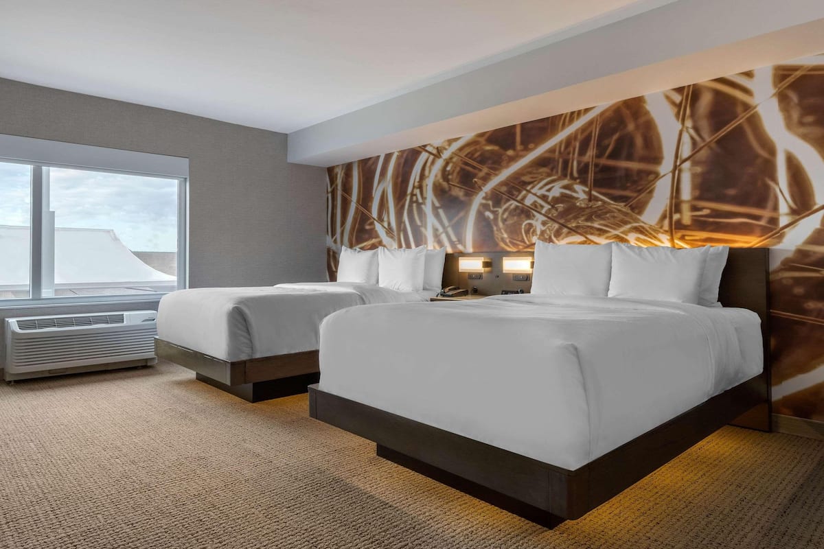 Quarto de hotel com duas camas, uma janela grande e design moderno na parede.