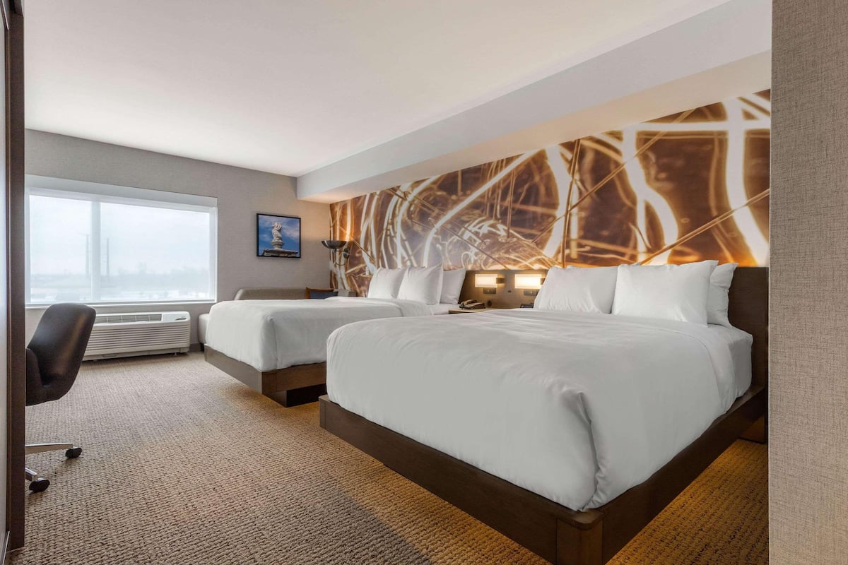 Quarto de hotel com duas camas, uma escrivaninha e uma janela grande.
