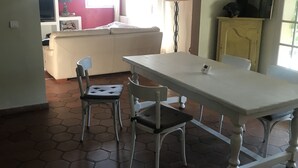 Ein Essbereich mit Tisch und zwei Stühlen, einer Couch und einem Fernseher im Hintergrund.