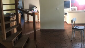 Eine Treppe führt zu einer zweiten Etage, ein Küchenbereich mit Fernseher und ein Sessel in einem Raum mit sechseckigem Fußbodenmuster.