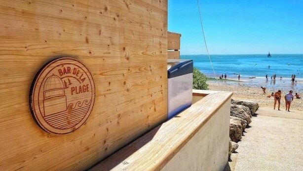 A wooden wall with a plaque reading "BAR DE LA PLAGE" and a view of a beach with people and a sailboat in the distance. - Quiet town house 2km from Ile de Ré bridge (La Rochelle)