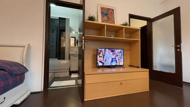 A compact room with a bed, a TV on a wooden stand, and a door leading to a bathroom. - ❤️CityCenter Rosetti Bohemian Rhapsody (București)