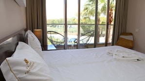 A hotel room with a bed, a window with a view of palm trees and a parking lot, and a chair outside the window. - Apartment Villa das Lagoas - By D´alma Portuguesa (Albufeira)
