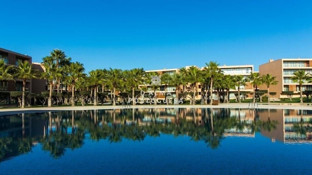 A hotel with a large reflective pool, palm trees, and modern buildings. - Apartment Villa das Lagoas - By D´alma Portuguesa (Albufeira)