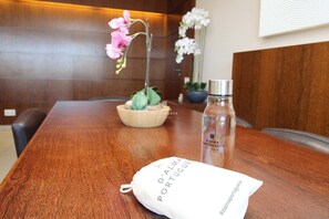 Una mesa de madera con un mantel blanco, una botella de D'Alma Portuguesa y una pequeña orquídea en maceta.