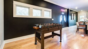 A modern room with a foosball table, a dining area with a table and chairs, and a window with decorative glass.
