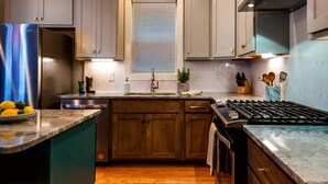 A modern kitchen with wooden cabinets, a stainless steel refrigerator, a built-in stove, and a window with blinds. - Elvis-themed Nashville home | sleeps 12, 4 bedrooms, patio & garage (Nashville)