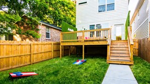 A backyard with a wooden deck, a concrete pathway, and a fenced area.
