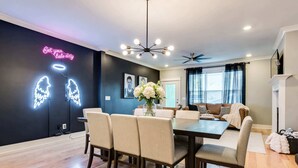 A modern living room with a dining area, featuring a black wall with neon signs, a chandelier, and a ceiling fan. - Elvis-themed Nashville home | sleeps 12, 4 bedrooms, patio & garage (Nashville)