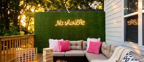 Ein gemütlicher Außenbereich mit einer Neonreklame mit dem Schriftzug „Nashville“, einer Holzterrasse und einer grünen Wand.
