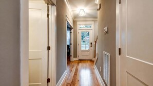 A hallway with wooden flooring, white walls, and a door leading to a room. - Elvis-themed Nashville home | sleeps 12, 4 bedrooms, patio & garage (Nashville)